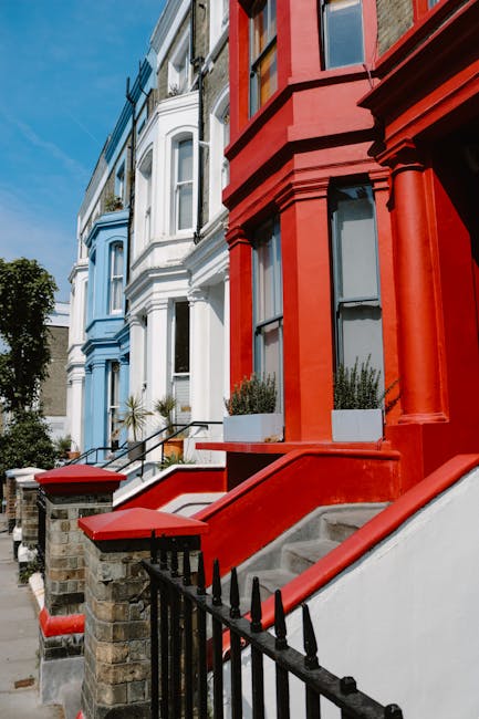 Image showing a row of multicoloured Victorian-style terraced houses with large bay windows and decorative cornices in Notting Hill, London, under a clear blue sky. In front of the houses, a Removal V