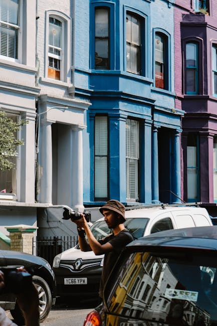 A row of brightly coloured Victorian terraced houses in Notting Hill with each property featuring bay windows, ornate white window framing, and small front gardens with potted plants and wrought iron 